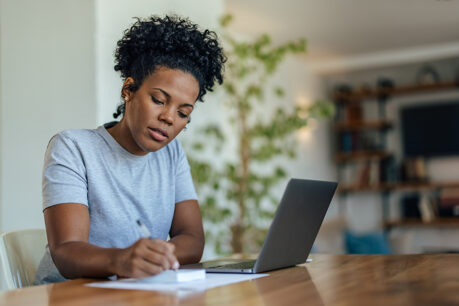 Woman sitting at home table reviewing notes and laptop