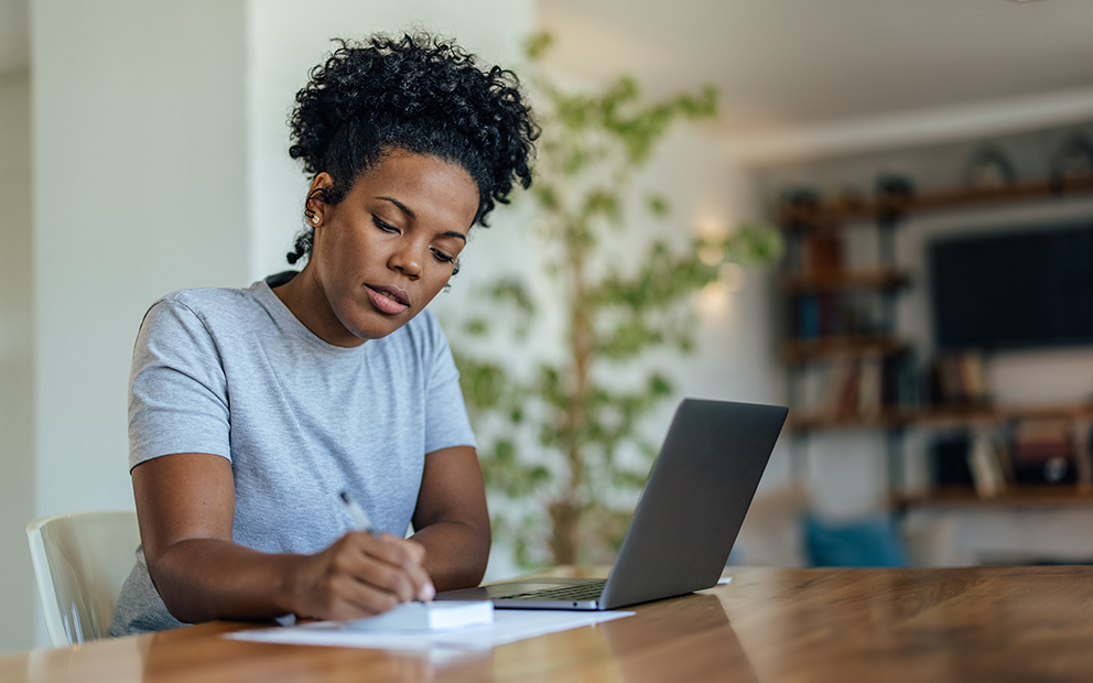 Woman sitting at home table reviewing notes and laptop