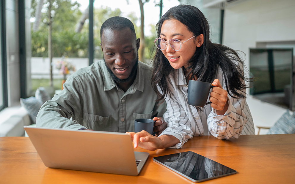 Man and woman couple looking at laptop together while they sit at kitchen table