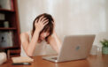 Woman has head in her hands while she looks at laptop screen
