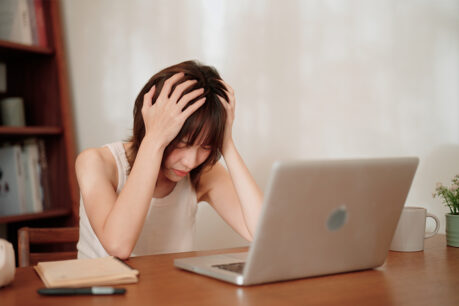 Woman has head in her hands while she looks at laptop screen