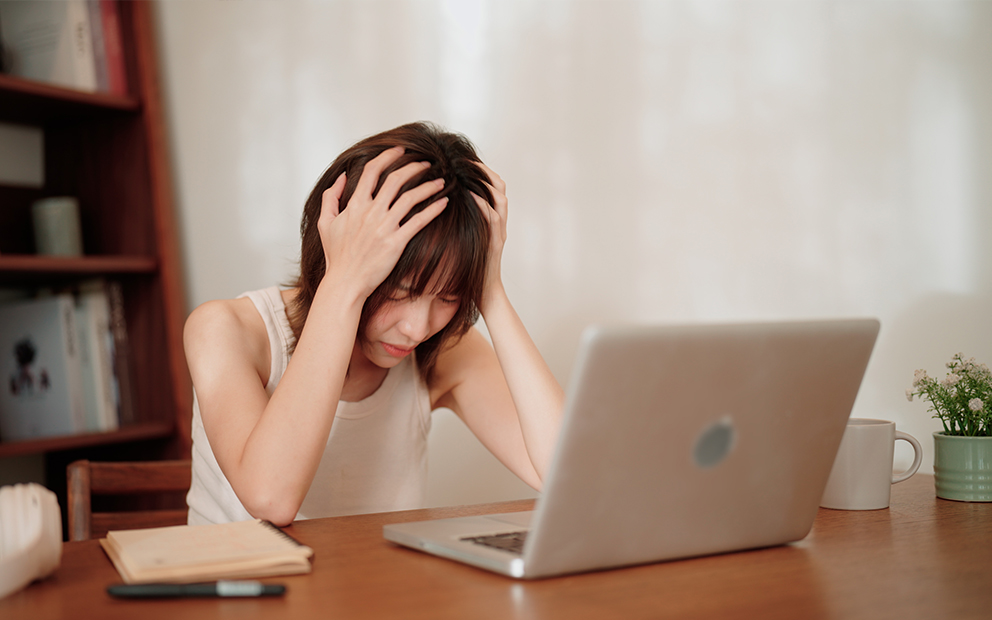 Woman has head in her hands while she looks at laptop screen