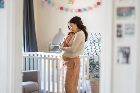 Mother holding newborn child while standing in at-home nursery