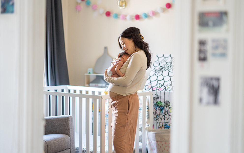 Mother holding newborn child while standing in at-home nursery