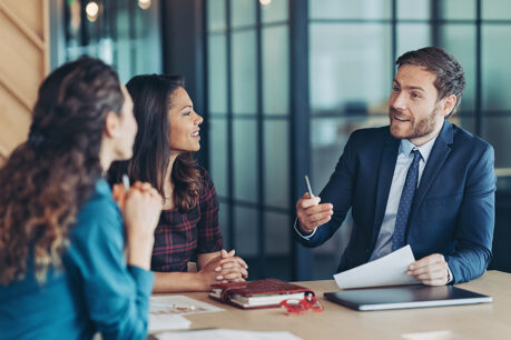 Man speaking to woman while they all sit at an office table together