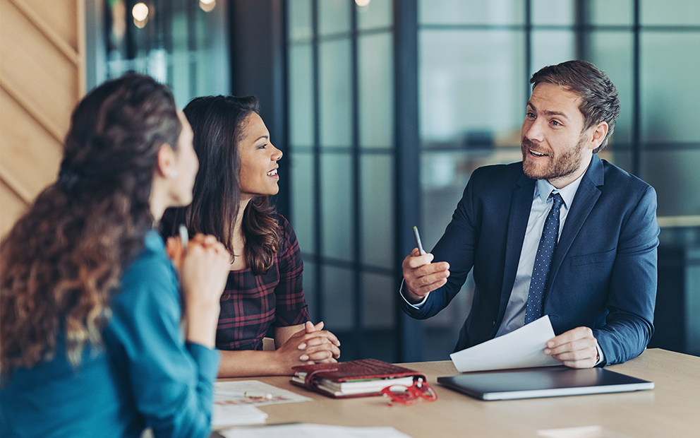 Man speaking to woman while they all sit at an office table together
