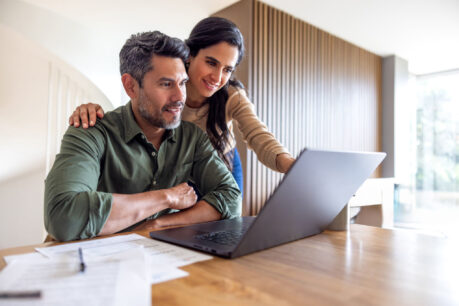 Couple sitting at kitchen table together while they look over laptop and documents