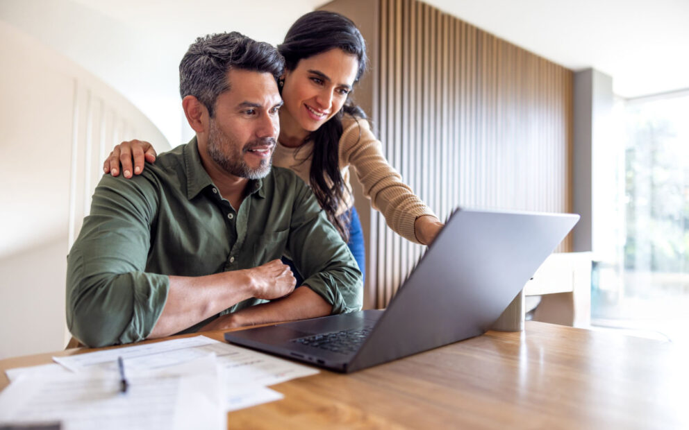 Couple sitting at kitchen table together while they look over laptop and documents