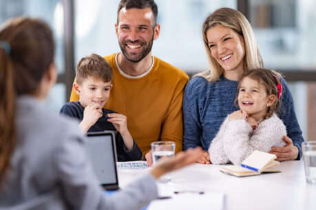 A wife and husband with their two young children sitting with an agent while the smile and talk together