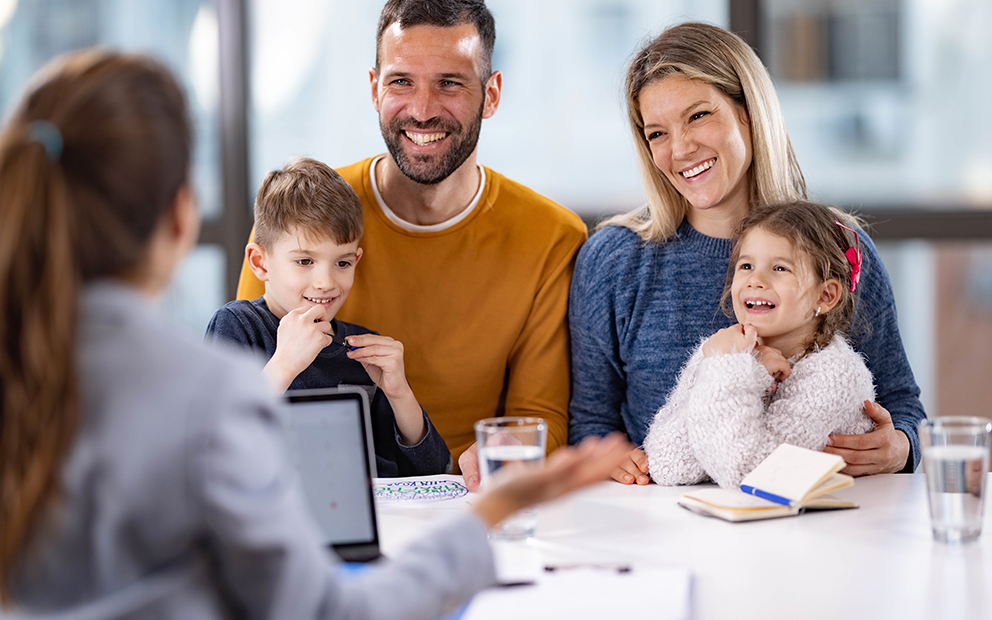 A wife and husband with their two young children sitting with an agent while the smile and talk together