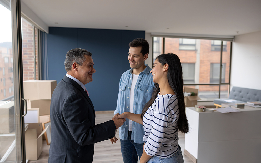 Young couple shaking hands with realtor in new home
