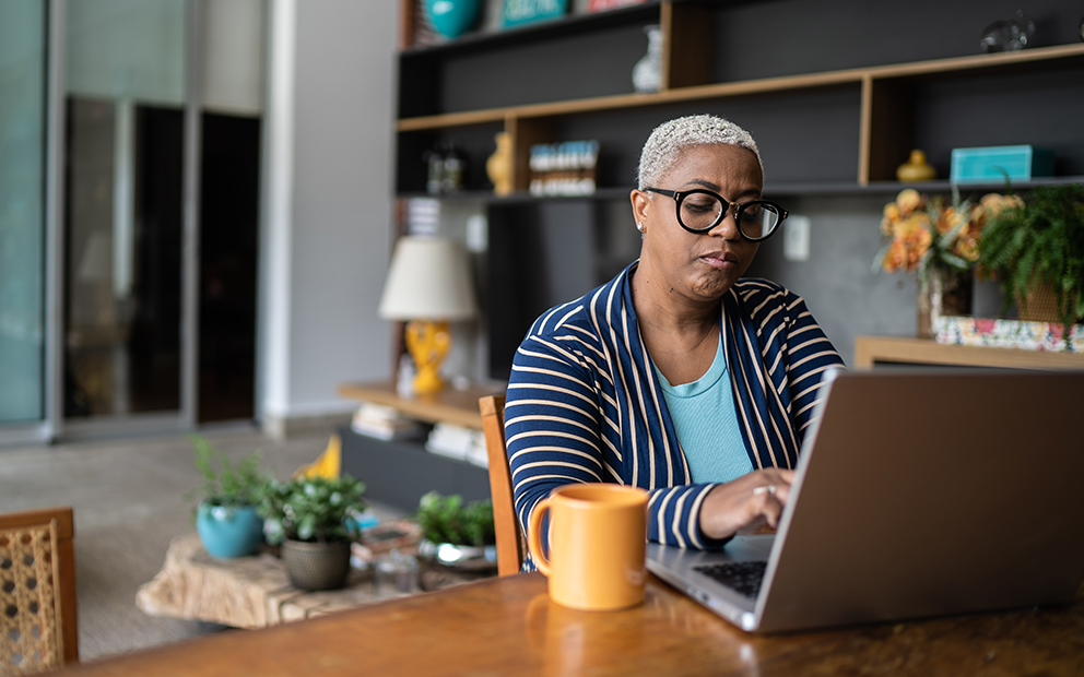 Woman sitting at kitchen table while looking at open laptop