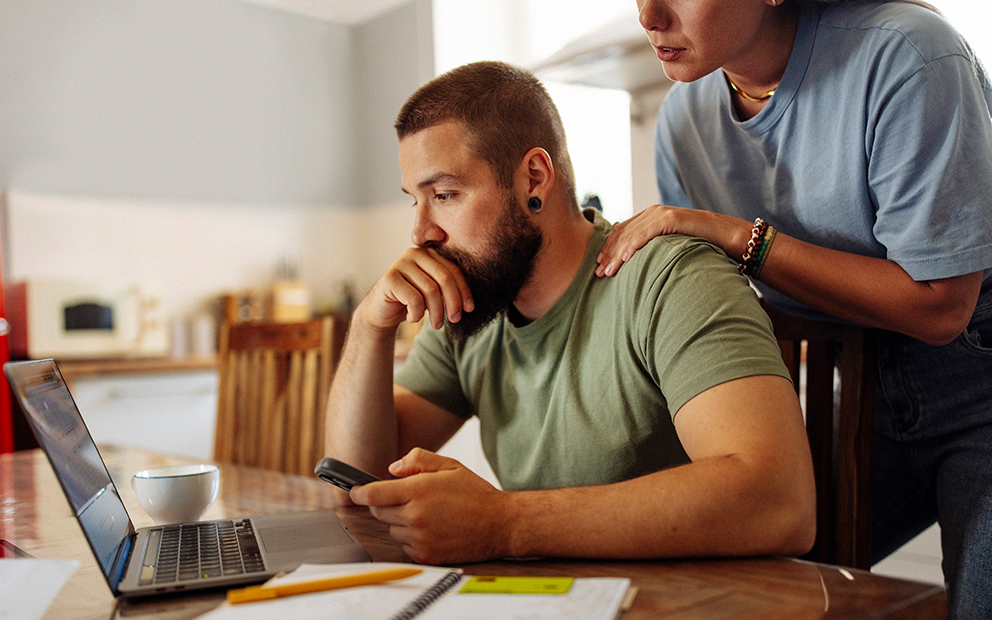 Man looking over info on laptop while sitting in home kitchen