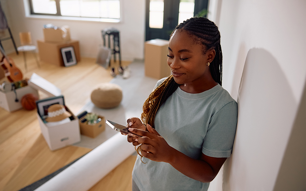 Youmg female adult researching info on cell phone while packing up home