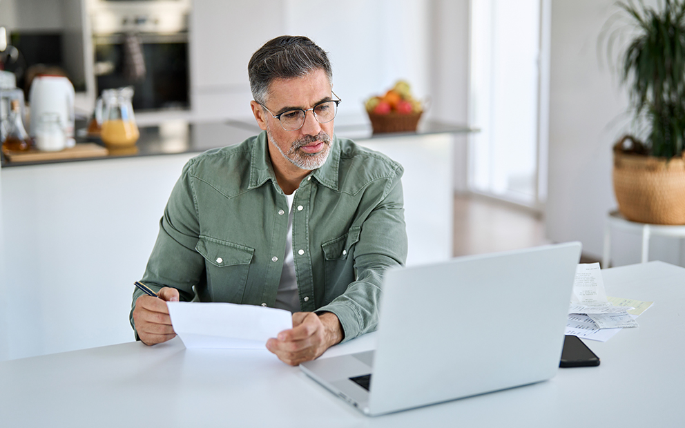 Middle aged man researching finances on laptop at home
