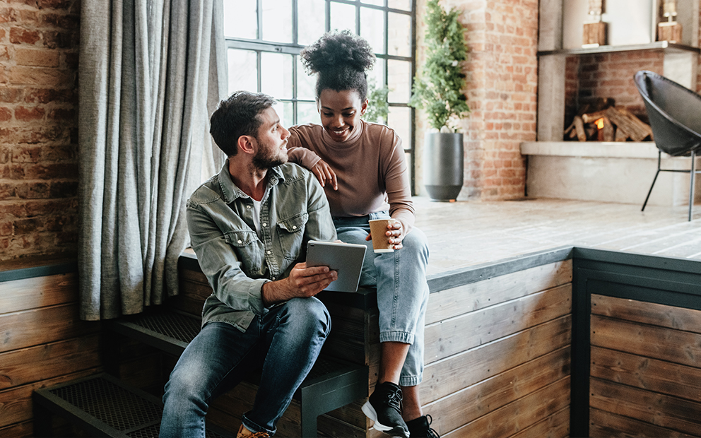 Young couple smiling and discussing while looking at tablet screen together