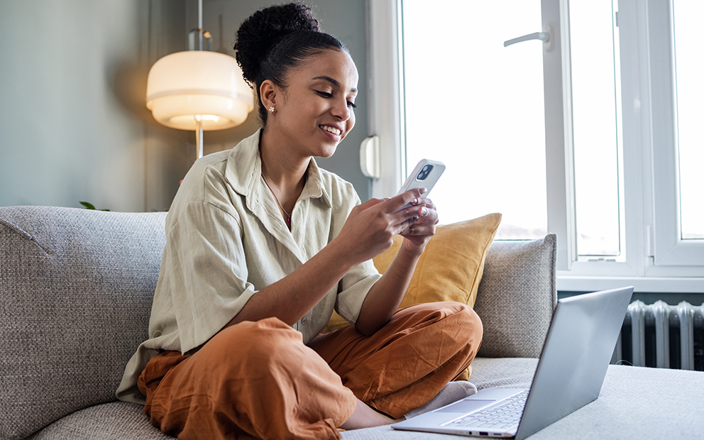 Young woman researching info on her phone and laptop at home