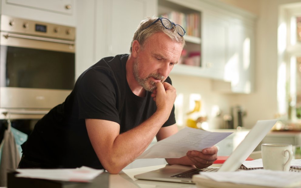 Older man looking at documents inside home kitchen to look into using Home equity without refinancing