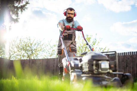 Man outside mowing lawn while wearing headphones during first summer in a new home