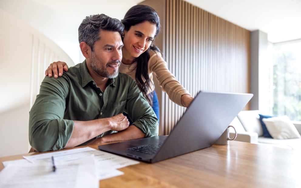 Adult man and woman couple looking at laptop at home to research are high interest checking accounts worth it