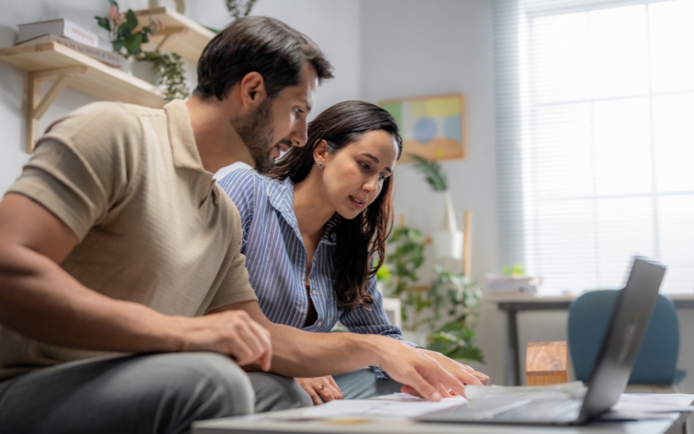 Young man and woman couple at home looking up VA refinance net tangible benefit on computer